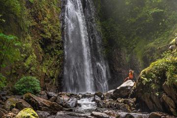 A person standing next to the largest waterfall at El Tigre Waterfalls in Monteverde, Costa Rica.